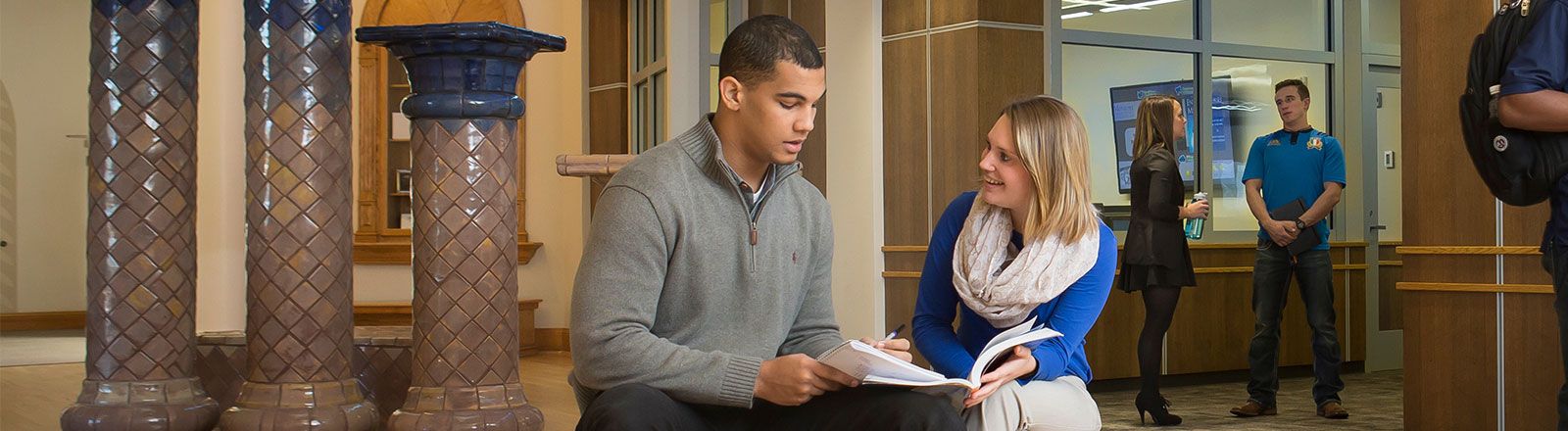 Two students sitting in lobby of Kepner Hall looking at book