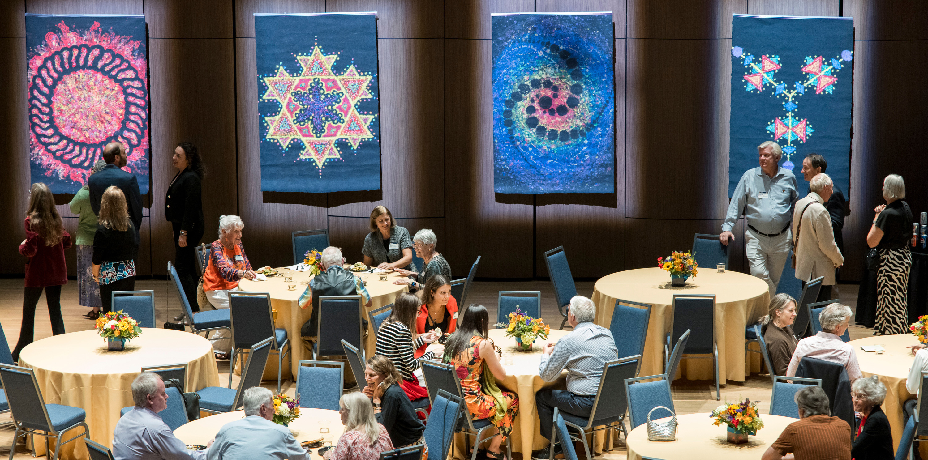 A group of people sitting at tables with artwork on the wall behind them