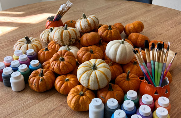 Multiple pumpkins on table with paint and brushes.