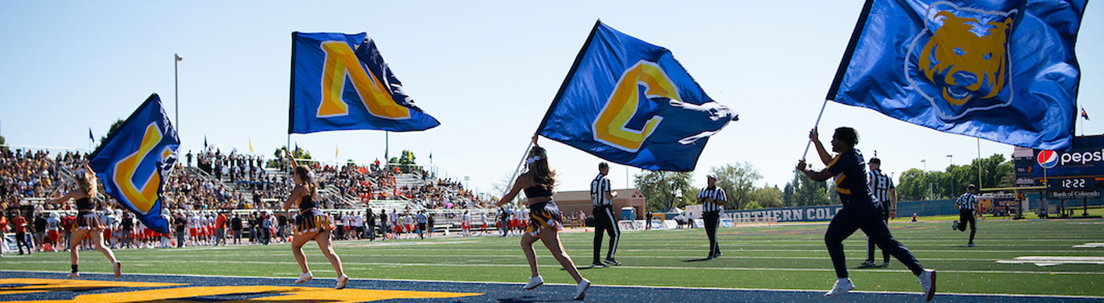 Cheerleaders running with flags that spell UNC in the endzone of the football field.