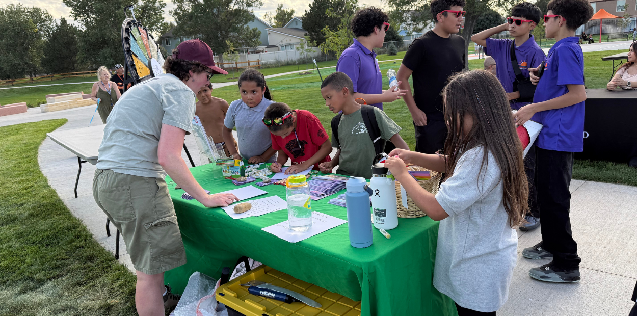 A member of the Generation Wild team talking with children at a table in the park.