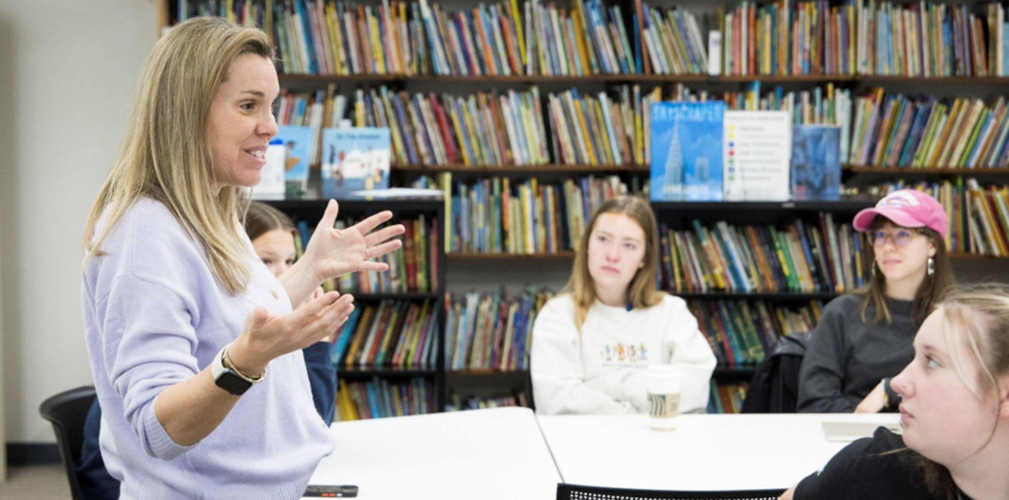 A professor smiling as she speaks to group of students in a library